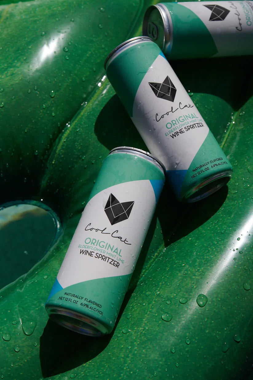 3 cans of Cool Cat Elderflower Sparkling Cocktail on a green floatie.