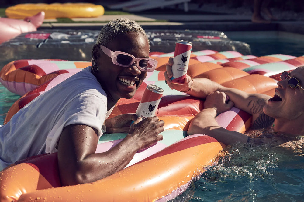 Two young people floating in pool while holding Cool Cat wine cocktails.