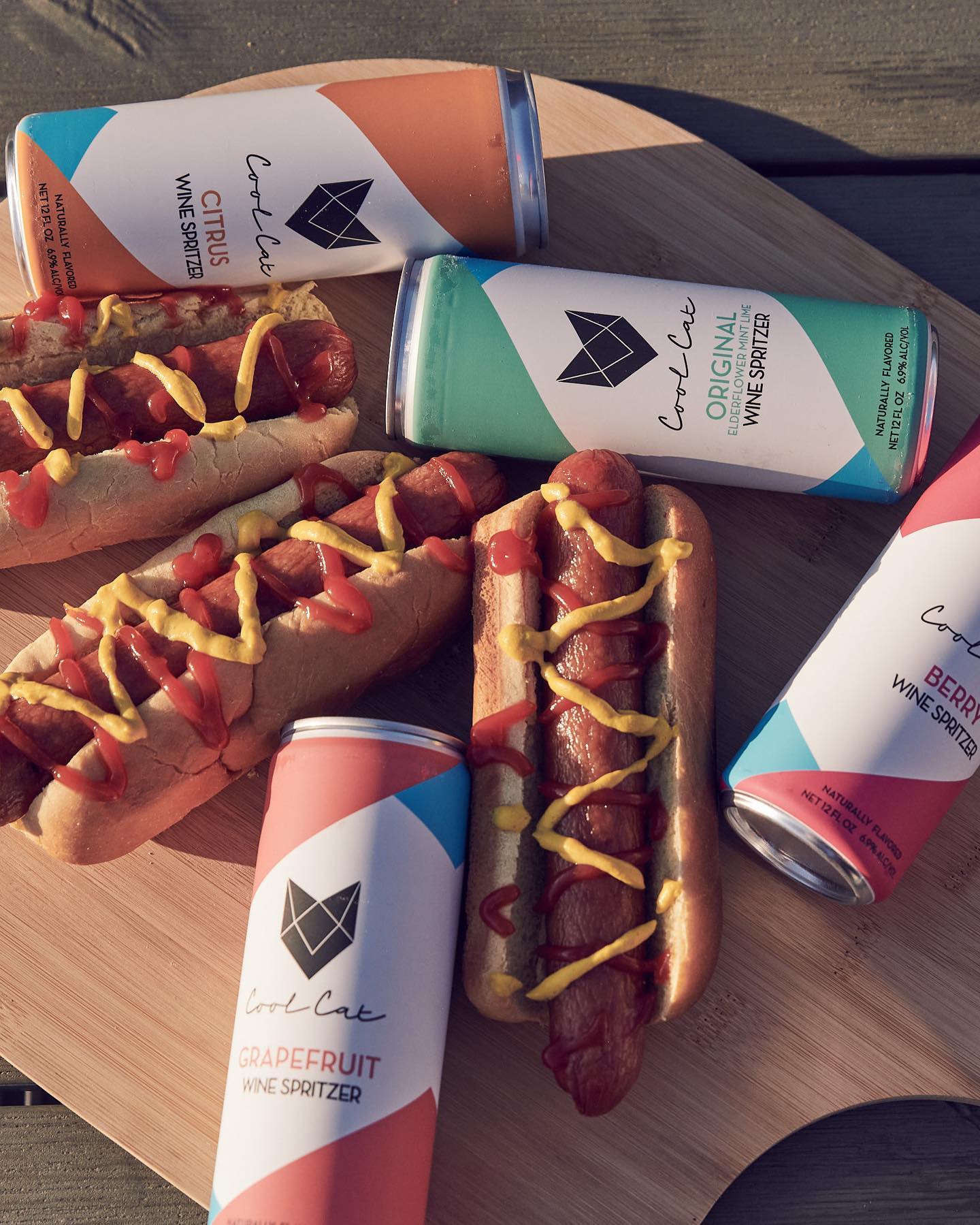 A variety of Cool Cat Wine Spritzers next to hot dogs at a barbecue.