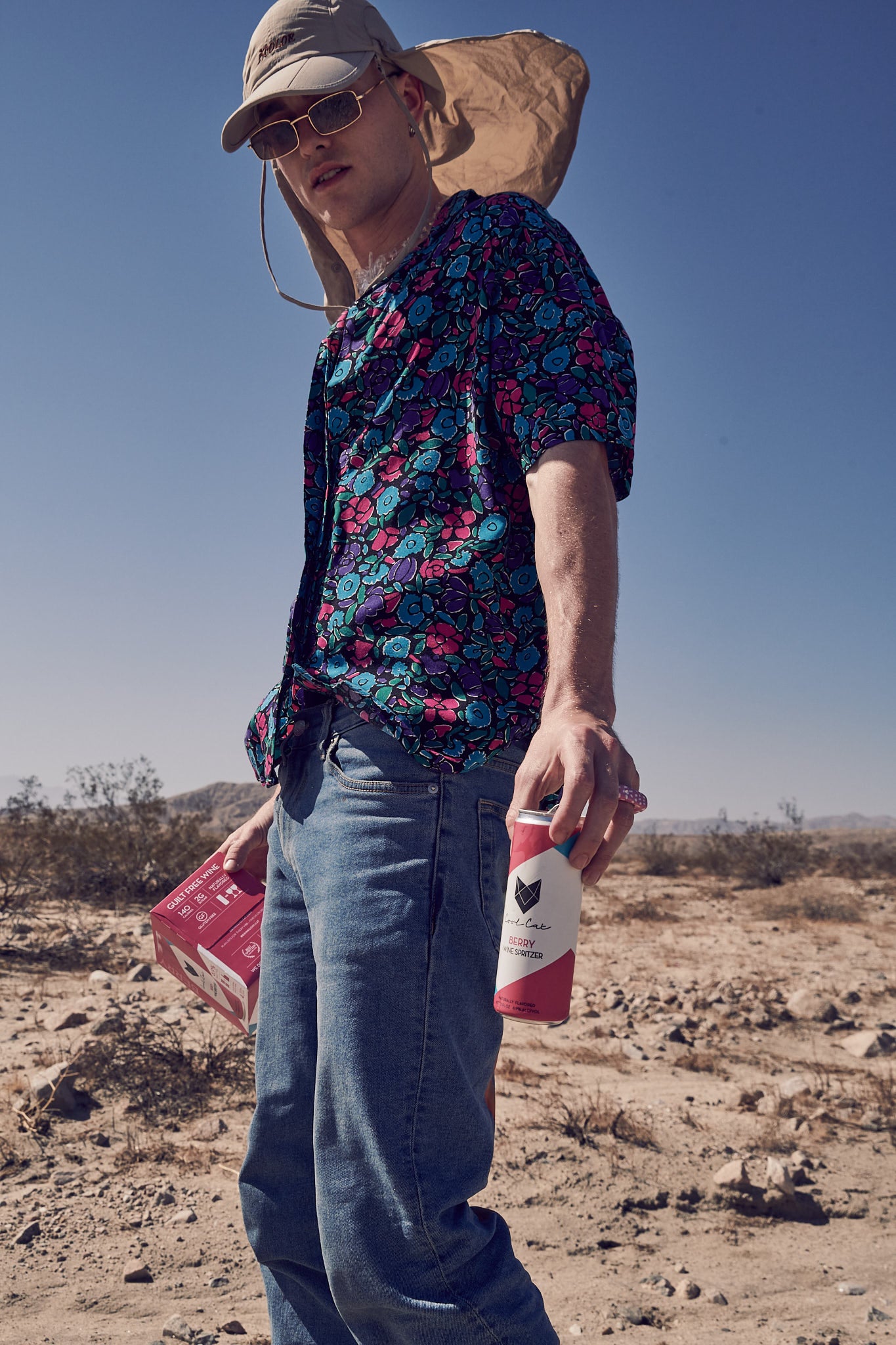 Dakota Griffin stands in the desert with a 4-pack of Berry Cool Cat Wine Spritzer.