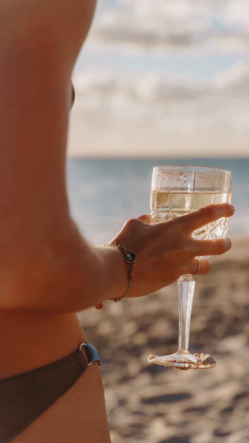 A woman holds a glass of Cool Cat Sparkling Cocktail at the beach.