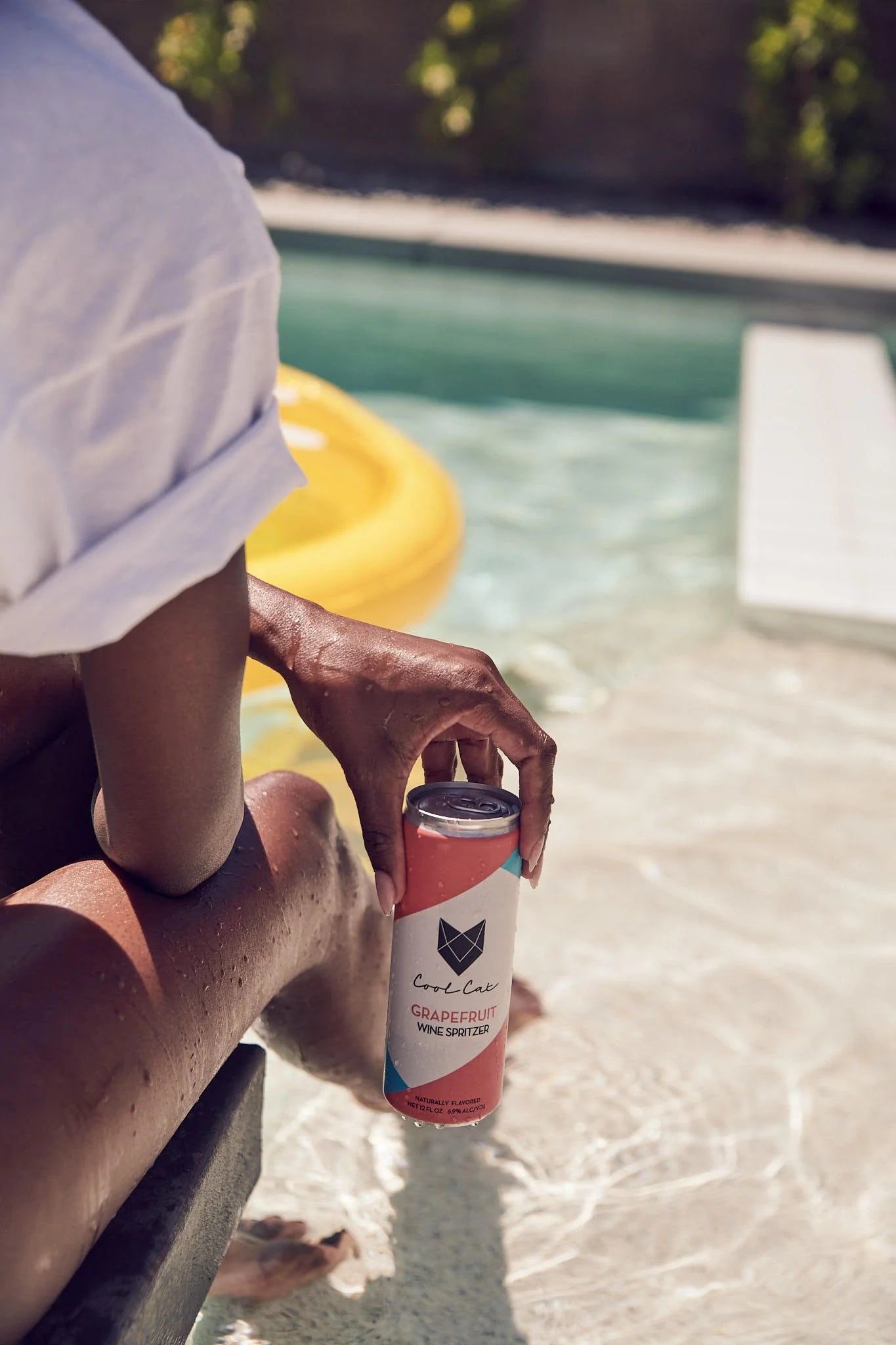 Someone holds a can of Cool Cat Grapefruit Sparkling Cocktail by the pool.